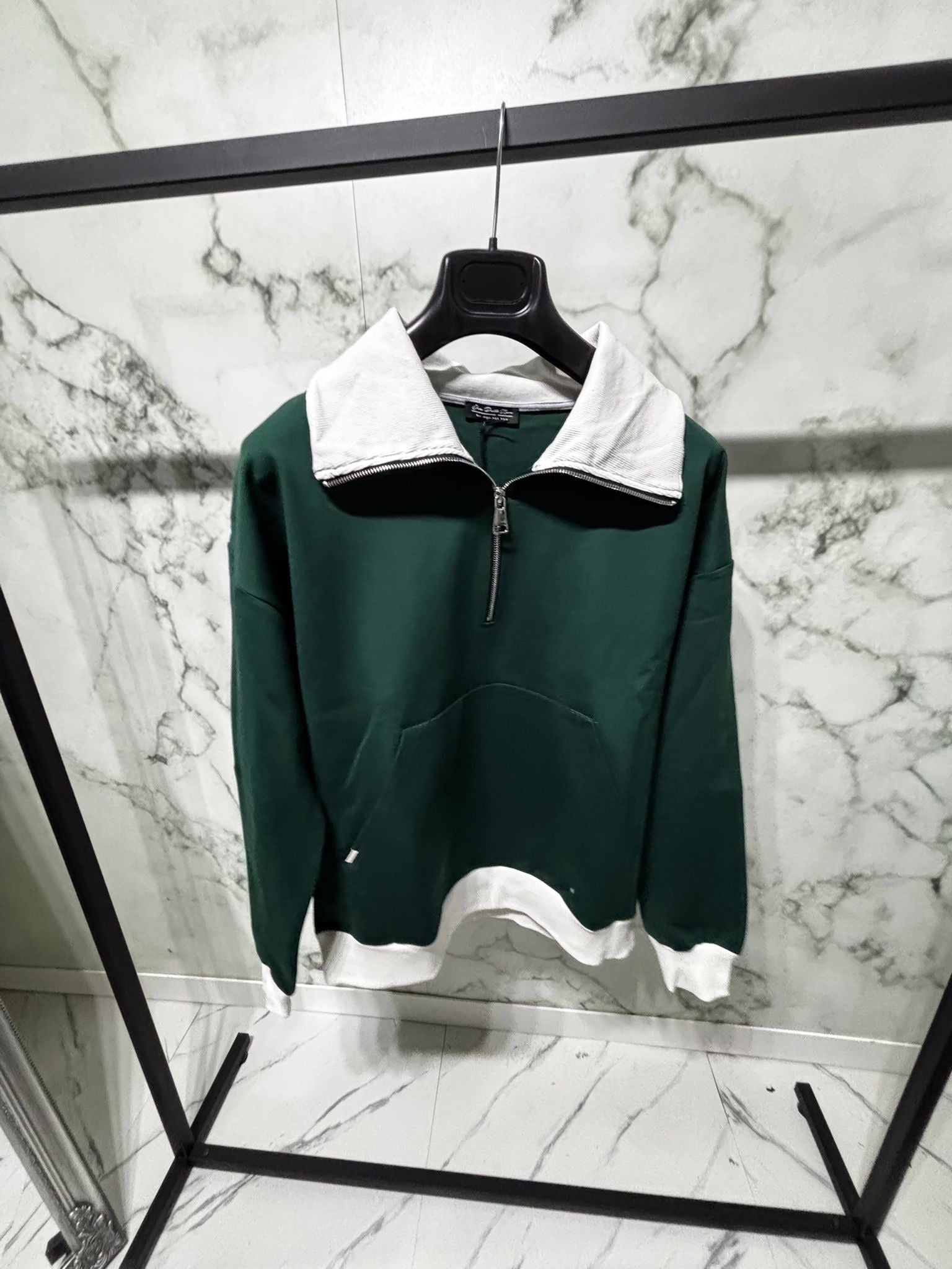 Forest Zip 2.0 Varsity Felpa in verde e bianco su appendiabiti, design bicolore con colletto a mezza zip e tasca a marsupio.