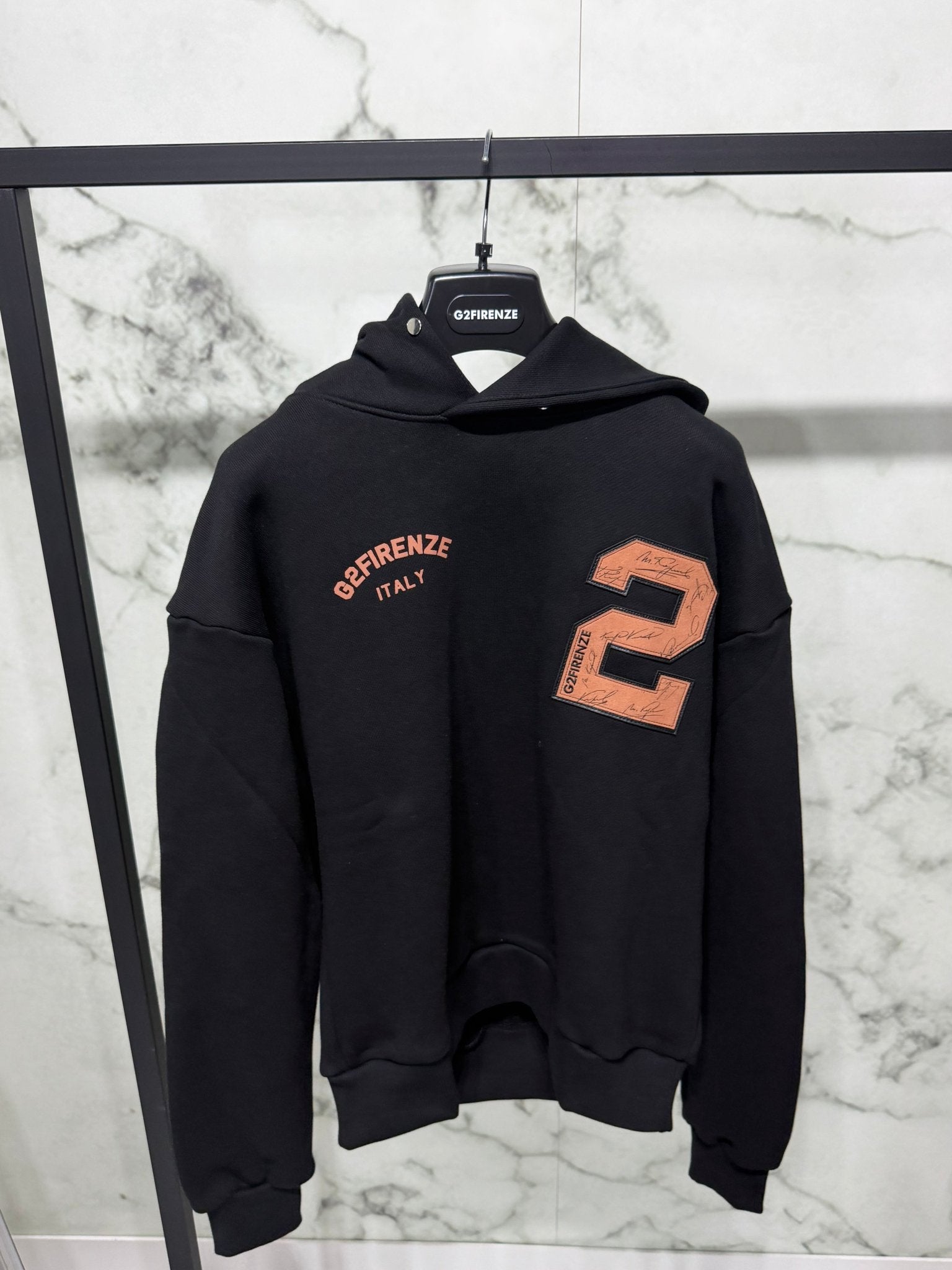 Felpa G2 Firenze “Signature Two” nera con maxi patch numero 2 e logo, ideale per outfit urban, esposta su appendiabiti in marmo bianco.